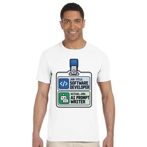 May include: A white t-shirt featuring a graphic of an ID badge. The badge displays the text JOB TITLE: SOFTWARE DEVELOPER with a code icon, and ACTUAL JOB: AI PROMPT WRITER with a robot icon. The badge has a blue clip at the top.