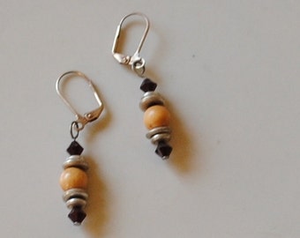 May include: A pair of dangle earrings with silver-tone lever-back closures. Each earring features a light orange bead, silver-tone metal rings, and dark red crystal accents. The earrings are displayed on a white surface.