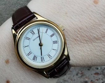 Vintage gold colour Sekonda ladies watch, round white roman numerals face, and burgundy brown leather strap.