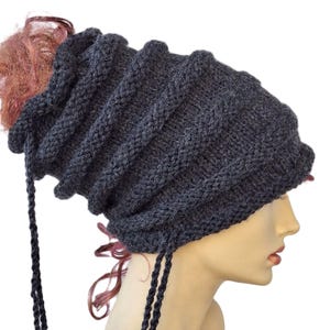 Peut inclure: Un bonnet en tricot gris avec un long porte-queue tressé. Le bonnet est à motif torsadé et est conçu pour être porté avec une queue de cheval.