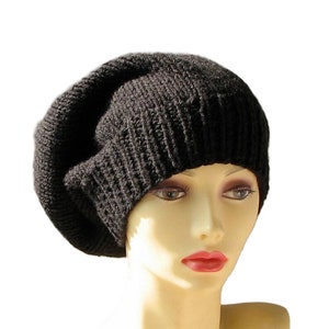 May include: A black knitted beanie hat with a ribbed texture. The hat is made of a soft, dark material and has a slouchy fit. The hat is displayed on a mannequin head against a white background.