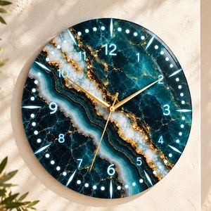May include: A round wall clock featuring a deep teal and white marble-like pattern with gold veining. The clock face displays white Arabic numerals from 1 to 12 and thin gold-coloured hour, minute, and second hands centred on the dial.