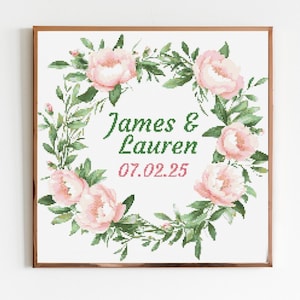 Może przedstawiać: Oprawiony wzór haftu krzyżykowego z kwiatowym wieńcem z różowych piwonii i zielonych liści. Imiona "James & Lauren" są w zielonym skrypcie, z datą "07.02.25" w kolorze różowym poniżej. Rama jest w ciepłym brązie.