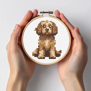 Peut inclure: Une broderie au point de croix représentant un chien assis sur un fond blanc. La broderie est encadrée dans un cercle en bois.