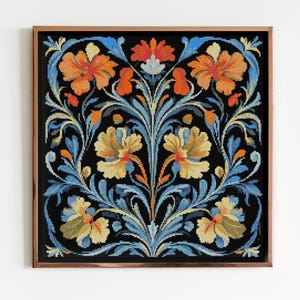 May include: A framed floral cross-stitch design. The artwork features a symmetrical pattern of orange, yellow, and blue flowers and foliage against a black background. The frame is a warm brown color.