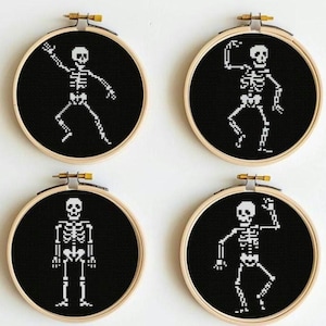 May include: Four round embroidery hoops with black fabric, each featuring a white cross-stitch skeleton in different poses. The hoops have wooden frames and brass hardware. A fun, spooky Halloween decoration.