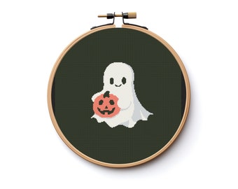 Puede incluir: Un fantasma blanco sosteniendo una calabaza naranja sobre un fondo verde oscuro. El fantasma tiene una cara sonriente y está sosteniendo la calabaza en sus brazos. La imagen está en un aro de bordado circular.