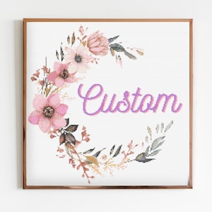 May include: A framed cross-stitch design featuring a floral wreath in shades of pink and brown, surrounding the word "Custom" in purple.