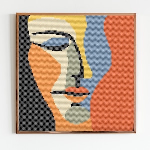 May include: A framed abstract portrait of a person's face with a black, yellow, orange, blue, and green color scheme. The portrait is made of small squares of fabric.