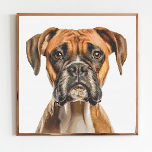 Puede incluir: Retrato en punto de cruz enmarcado de un perro Boxer. El perro tiene un pelaje marrón y blanco, con un hocico negro y orejas caídas. El perro mira directamente al espectador. El marco es de color marrón oscuro.