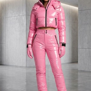 May include: A shiny pink cropped puffer jacket with a hood and black zip, paired with matching high-waisted quilted trousers, pink gloves, and pink lace-up boots. The ensemble features a glossy finish and black accents on the zips and cuffs.