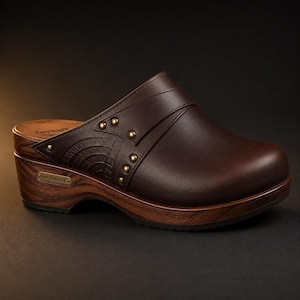 Può includere: Uno zoccolo marrone scuro con suola platform effetto venatura del legno, caratterizzato da una tomaia in pelle liscia, borchie decorative color ottone e un motivo semicircolare in rilievo sul lato. Una piccola targhetta metallica e il plantare riportano la scritta FancyStorePK.