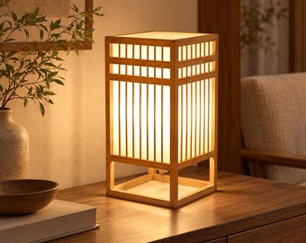 May include: A rectangular table lamp featuring a light-colored wooden frame with a grid-like lattice structure. The lamp has a translucent white shade that emits a warm, soft glow, illuminating the vertical wooden slats of the frame.