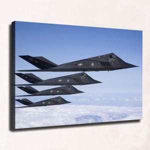 May include: A canvas print featuring four black F-117 Nighthawk stealth aircraft flying in a staggered formation against a clear blue sky above a layer of white clouds. Each angular jet displays visible United States military insignia.