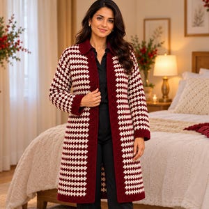 Könnte beinhalten: Eine lange, offene Strickjacke mit einem sich wiederholenden geometrischen Muster in tiefem Burgunderrot und Creme. Das Kleidungsstück hat einen einfarbigen burgunderroten Kragen, lange Ärmel und einen geraden Saum unter der Hüfte.