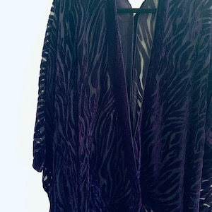 May include: A dark purple velvet kimono with a zebra print pattern. The kimono has a deep V-neck and long sleeves.