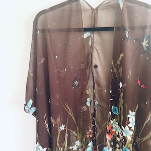 May include: A brown sheer kimono with a floral print featuring butterflies, flowers, and leaves. The kimono has a V-neck and short sleeves.