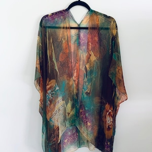 K&ouml;nnte beinhalten: Ein durchsichtiges, leichtes Kimono mit einem farbenfrohen, abstrakten Blumenmuster in Braun-, Gr&uuml;n-, Orange- und Lilat&ouml;nen. Das Kimono hat einen V-Ausschnitt und eine lockere, flie&szlig;ende Passform.