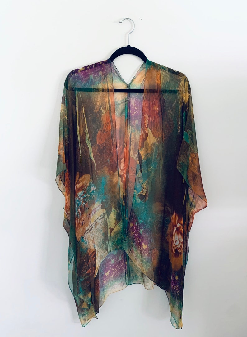 K&ouml;nnte beinhalten: Ein durchsichtiges, leichtes Kimono mit einem farbenfrohen, abstrakten Blumenmuster in Braun-, Gr&uuml;n-, Orange- und Lilat&ouml;nen. Das Kimono hat einen V-Ausschnitt und eine lockere, flie&szlig;ende Passform.