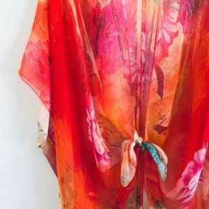 K&ouml;nnte beinhalten: Ein rotes, orangefarbenes und rosafarbenes Kimono mit floralem Muster und einem Bindeverschluss. Das Kimono ist aus einem durchsichtigen Stoff gefertigt und hat eine lockere, flie&szlig;ende Passform.