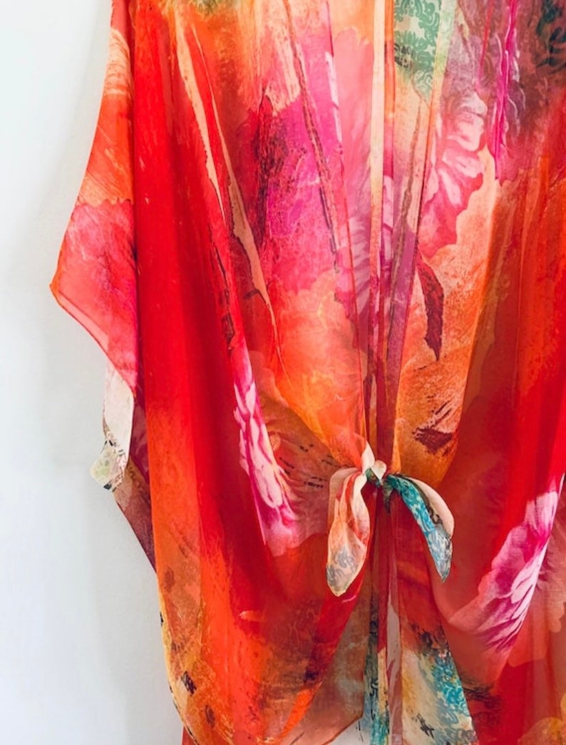 K&ouml;nnte beinhalten: Ein rotes, orangefarbenes und rosafarbenes Kimono mit floralem Muster und einem Bindeverschluss. Das Kimono ist aus einem durchsichtigen Stoff gefertigt und hat eine lockere, flie&szlig;ende Passform.