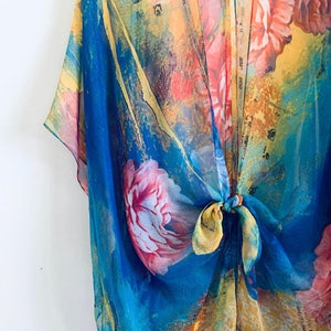 K&ouml;nnte beinhalten: Ein durchsichtiger Kimono mit floralem Druck in Blau, Gelb und Rosa mit einem Bindeverschluss.