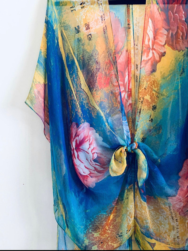 K&ouml;nnte beinhalten: Ein durchsichtiger Kimono mit floralem Druck in Blau, Gelb und Rosa mit einem Bindeverschluss.
