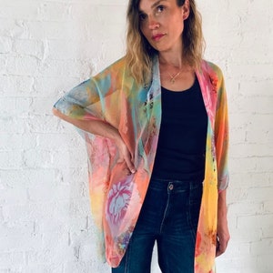 K&ouml;nnte beinhalten: Eine Frau tr&auml;gt einen durchsichtigen Kimono mit buntem Blumenmuster, ein schwarzes Tanktop und eine blaue Jeans.