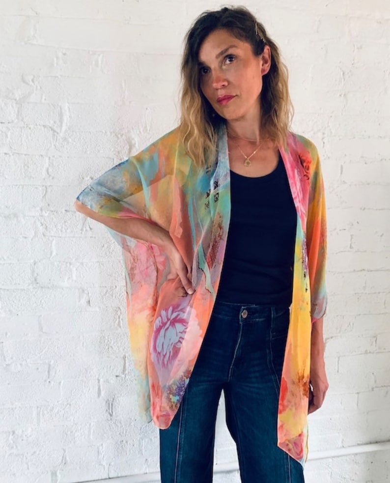 K&ouml;nnte beinhalten: Eine Frau tr&auml;gt einen durchsichtigen Kimono mit buntem Blumenmuster, ein schwarzes Tanktop und eine blaue Jeans.