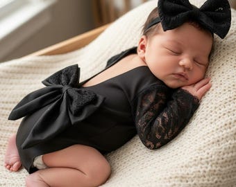 May include: A black long-sleeved bodysuit featuring lace sleeves and a large decorative bow on the back, paired with a matching black lace bow headband. The garment is solid black with intricate lace detailing on the sleeves and the back bow.