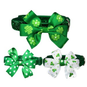 May include: Three green glitter dog collars with shamrock print bows. The bows are tied in a bow shape. The collars are for small dogs.