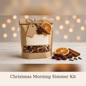 May include: A brown paper pouch containing dried fruit and spices, labeled Christmas Morning Simmer Kit. The pouch is tied with twine and decorated with a dried orange slice, a cinnamon stick, and a star anise, with more nearby.