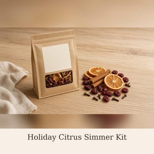 May include: A brown paper pouch with a clear rectangular window containing dried orange slices, cinnamon sticks, cranberries, and cloves. A blank white label is centered on the front of the pouch. Loose ingredients are arranged to the right.