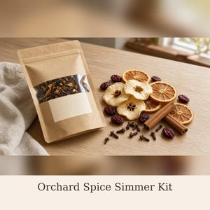 May include: A brown paper pouch with a clear window containing dried fruit and spice mix, labeled Orchard Spice Simmer Kit. Beside the pouch are dried apple slices, orange slices, cinnamon sticks, cloves, and red berries.