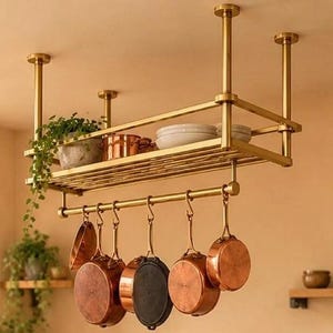 May include: A ceiling-mounted brass pot rack featuring a rectangular shelf holding a potted plant and white bowls, with a lower bar supporting five hanging copper-toned pans and pots of varying sizes, all suspended by four vertical metal rods.