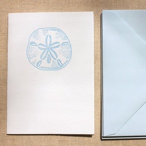 May include: A white card with a light blue sand dollar design. The card is blank and comes with a light blue envelope.