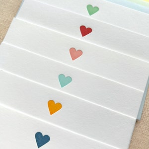 May include: Set of eight blank note cards with a heart cut-out in different colors: green, red, pink, blue, orange, and navy blue.