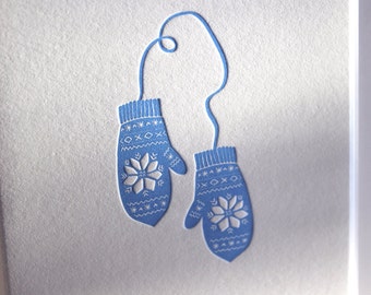 May include: A pair of blue knitted mittens with white snowflake designs, connected by a white string.