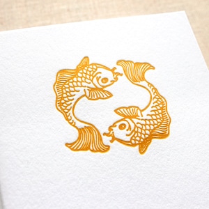 May include: Two gold-colored fish swimming in a circle, a traditional symbol of good luck and prosperity.