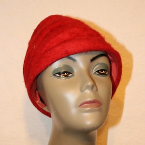May include: A red felt hat with a rounded crown and a wide brim. The hat is worn on a mannequin's head.