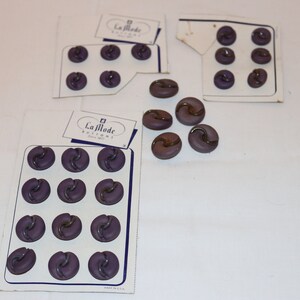 May include: A card of purple buttons with a gold swirl design. The card reads "La Mode Buttons".