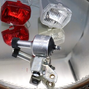 K&ouml;nnte beinhalten: Drei Fahrradlichter, eines rot, eines wei&szlig; und eines silberfarben mit dem Wort "UNION" darauf. Die Lichter befinden sich auf einer spiegelnden Oberfl&auml;che.