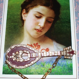 May include: A silver and red jeweled brooch shaped like a mandolin with a gold chain attached.