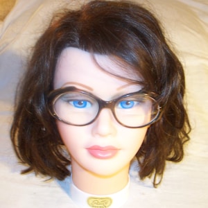 May include: A mannequin head with brown hair wearing black cat-eye glasses with blue lenses.
