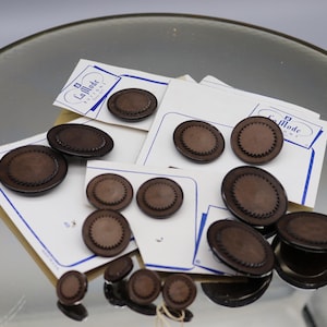 May include: A collection of brown plastic buttons with a decorative edge. The buttons are arranged on white paper with the text "La Mode" printed on the paper.