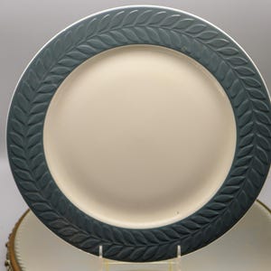 Op de afbeelding: Een grote, witte keramische dinerbord met een donkerblauwe rand met een herhalend bladontwerp.