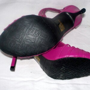 May include: A pair of pink high-heeled sandals with black soles and straps. The sandals have a textured sole.