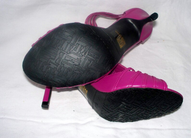 May include: A pair of pink high-heeled sandals with black soles and straps. The sandals have a textured sole.