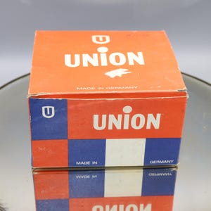K&ouml;nnte beinhalten: Eine rote und blaue Schachtel mit dem Wort "UNION" in wei&szlig;en Buchstaben darauf. Die Schachtel ist in Deutschland hergestellt und hat ein kleines "U"-Logo an der Seite.