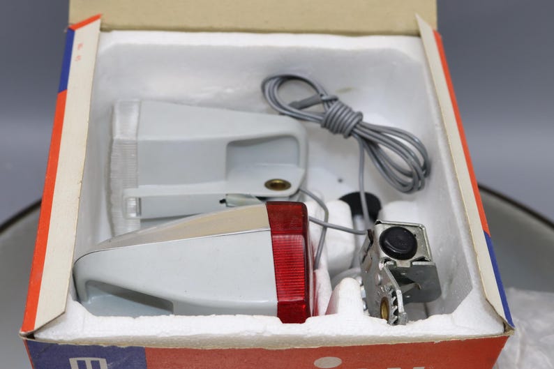 K&ouml;nnte beinhalten: Ein Satz mit zwei Fahrradlichtern in einer wei&szlig;en Box. Die Lichter sind wei&szlig; mit roten Reflektoren und werden mit einem Kabel zum Verbinden geliefert.